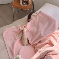 a woman laying on top of a bed under a pink blanket