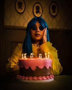 a woman with blue hair sitting in front of a birthday cake that has candles on it