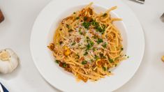 a white plate topped with pasta and parmesan cheese next to garlic, pepper shakers and utensils