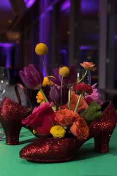 a pair of red high heeled shoes sitting on top of a table with flowers in it