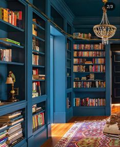 a room filled with lots of blue bookshelves and a chandelier hanging from the ceiling