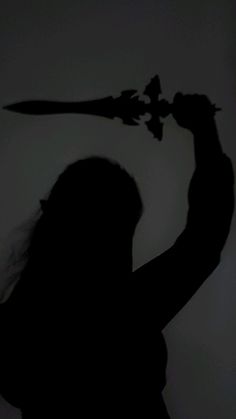 the shadow of a woman holding a knife in front of her head with one hand