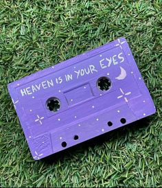 an old purple cassette with the words heaven is in your eyes written on it, laying on some green grass