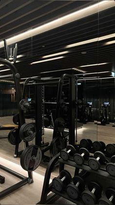 an empty gym with rows of weight machines and barbells in the foreground