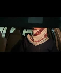 a woman wearing a scarf sitting in the back seat of a car with her head down