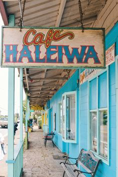 a bench sitting on the side of a sidewalk next to a blue building with a sign that says cafe halewa