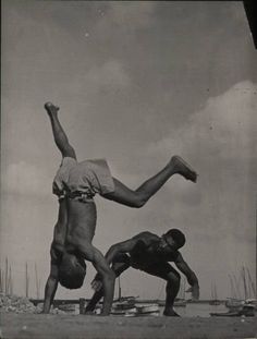 two men doing tricks on the beach with their hands in the air while another man watches