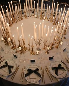 a white table topped with lots of plates and silverware next to candles in the middle