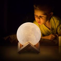 a young boy is looking at the moon lamp in front of him on a table