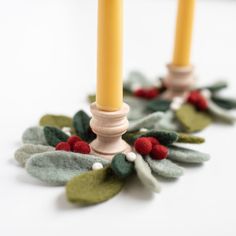 two candles that are sitting next to each other with leaves and berries on the candle holders