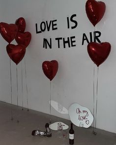 some red heart shaped balloons are in front of a sign that says love is in the air