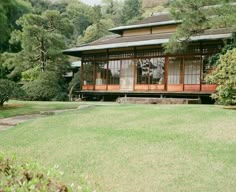 an old japanese style house in the middle of a field with trees and bushes around it