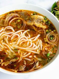 a bowl of soup with noodles, meat and veggies in it on a table