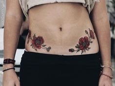 a woman's stomach with red flowers and leaves on her side, while wearing black pants