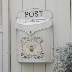 a white mailbox mounted to the side of a wooden wall next to a flower pot