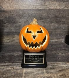 a carved pumpkin sitting on top of a wooden table next to a plaque that says halloween