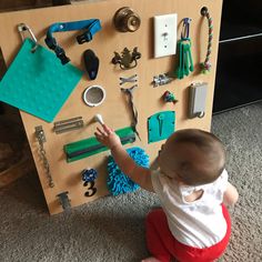 a baby sitting on the floor next to a wooden board with toys and magnets