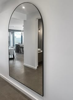 an arched mirror in the middle of a white walled room with a table and chairs