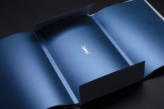 an open blue book with a small logo on the front and back cover, sitting on a black surface