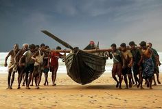 a group of people standing around a boat on the beach