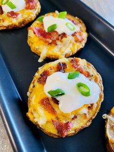 mini pizzas with cheese and green onions on a black tray, ready to be eaten