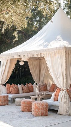 an outdoor seating area with white canopy and orange pillows on the floor, surrounded by trees