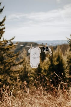 a baby's bodysuit hanging on a clothes line in front of some trees