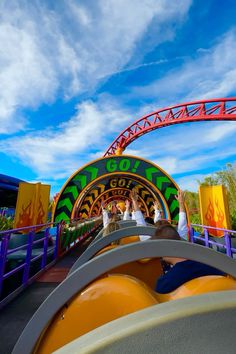 two people riding on a roller coaster at an amusement park with blue skies in the background