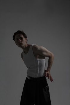 a man in white tank top and black pants posing for a photo with his hand on his hip