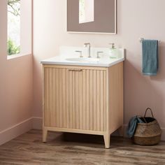 a bathroom with pink walls and wooden flooring has a mirror above the sink that is hanging on the wall