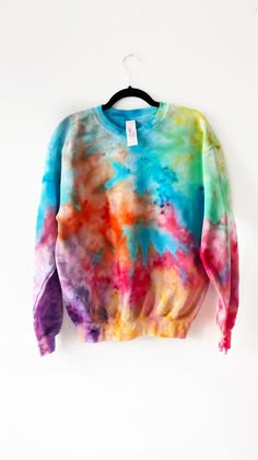 a colorful tie - dyed sweater hanging on a hanger against a white wall,