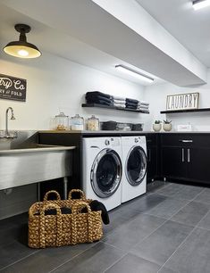 a washer and dryer in a small room with black cabinets, white walls and gray tile flooring