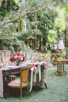 a table set up for a wedding with flowers and candles on it, surrounded by greenery