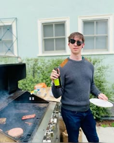 a man standing in front of a bbq grill holding a bottle of beer and a plate