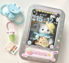 a small white teddy bear sitting in a miniature clock with other toy items around it