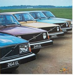 five old cars are parked in a row on the dirt road near an open field