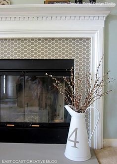 a white vase sitting on top of a table next to a black fire place mantle