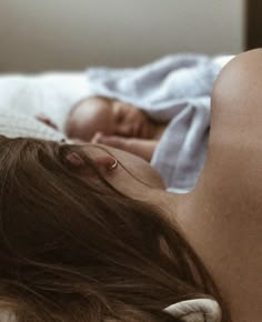 a woman laying on top of a bed next to a baby in her arms and head