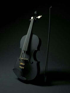 a black violin is sitting next to a stick on a dark surface with light coming from it