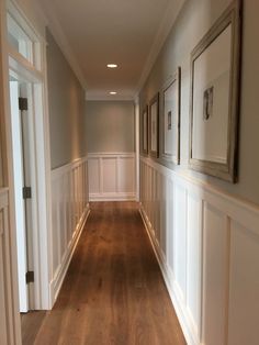 an empty hallway with framed pictures on the wall and hard wood flooring, along with white waives