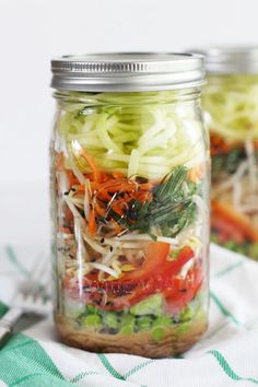 two mason jars filled with vegetables on top of a green and white table cloth next to a fork