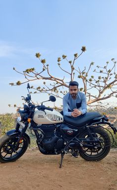 a man sitting on top of a motorcycle in front of a tree with no leaves