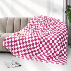 a pink and white checkered blanket sitting on top of a couch next to a potted plant