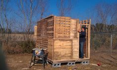 a man standing in the doorway of a wooden structure made out of wood pallets