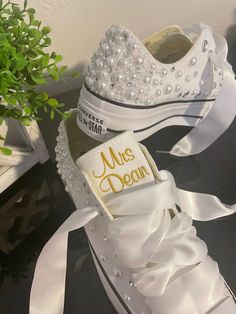 a pair of white shoes with pearls on them and a plant in the corner next to it