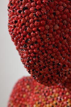 a red sculpture with lots of black dots on it's face and neck, in front of a white background