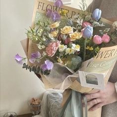 a woman holding a bouquet of flowers in front of a white wall with pictures on it