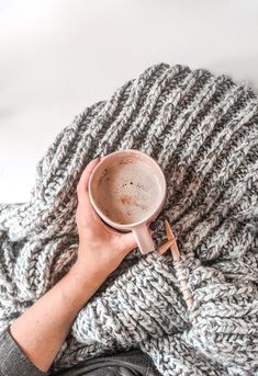 a person holding a cup of coffee on top of a blanket