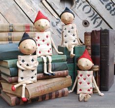 three clay figurines sitting on top of books and wearing red hats, one with his arms around the other's head