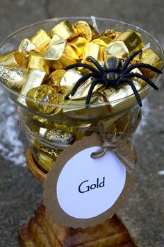 a glass bowl filled with gold candy and a spider sitting on top of the jar